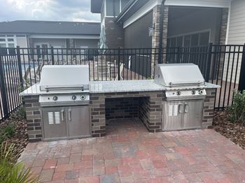 A brick BBQ grill with a white top is in the middle of a brick patio.